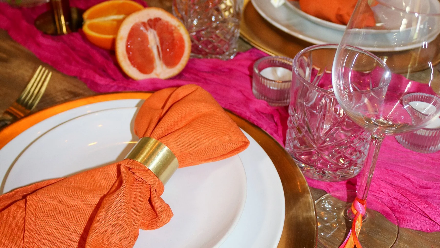 Kleurrijke Maeve dinerstyling met oranje servetten, roze bloemen en citrus