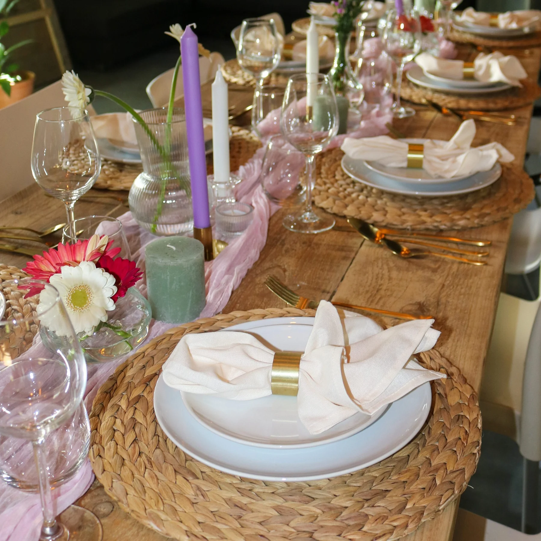 Gedekte tafel met lila kaarsen, pastelbloemen en rieten onderborden