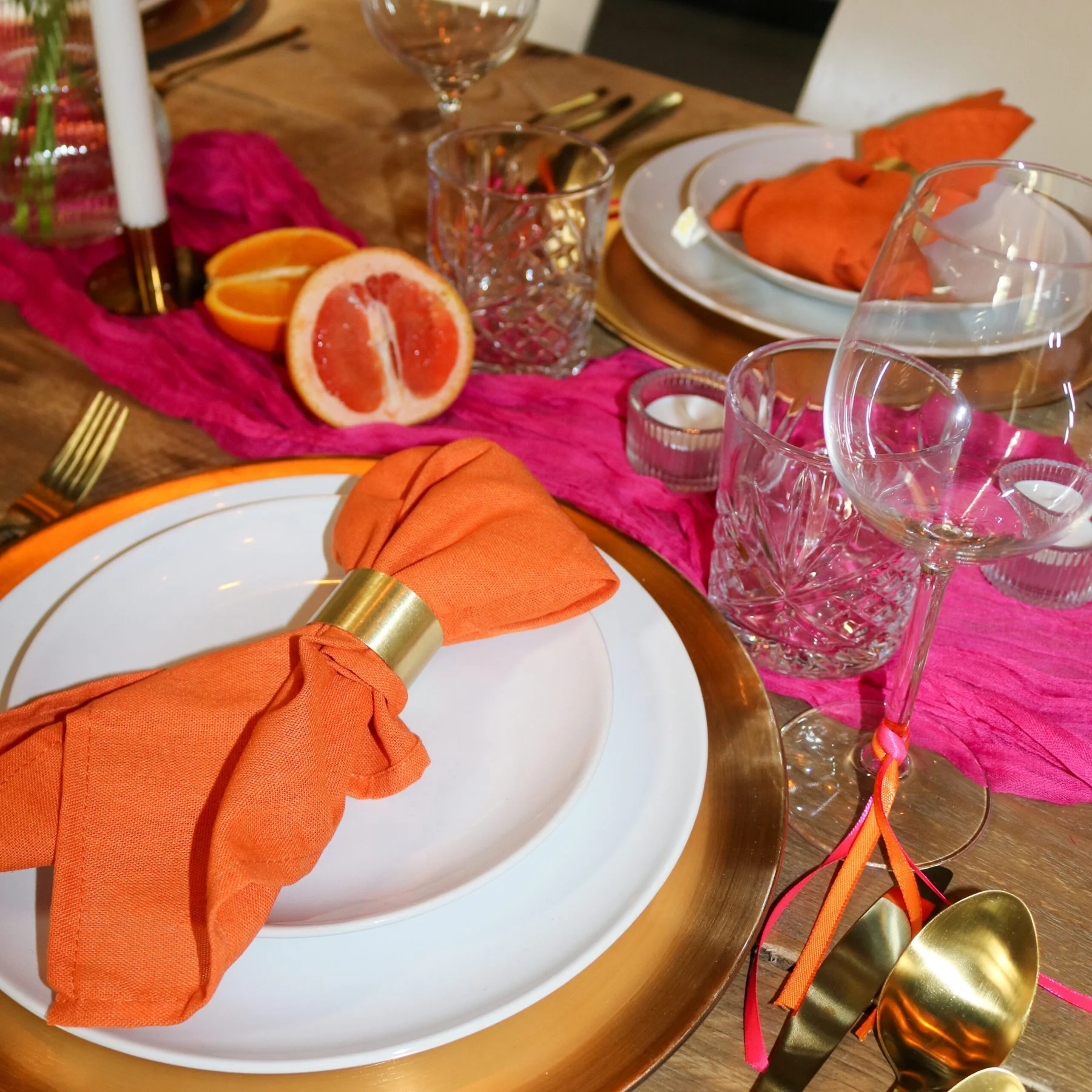 Roze tafelloper met oranje servetten, citrus en goudkleurig bestek